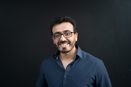 The shot of a happy man with smile on his face wearing eyeglasses looking at camera with black background.