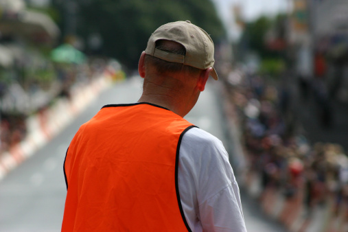 Back view of the orange safety vest of a street race marshall. Race track in background.
