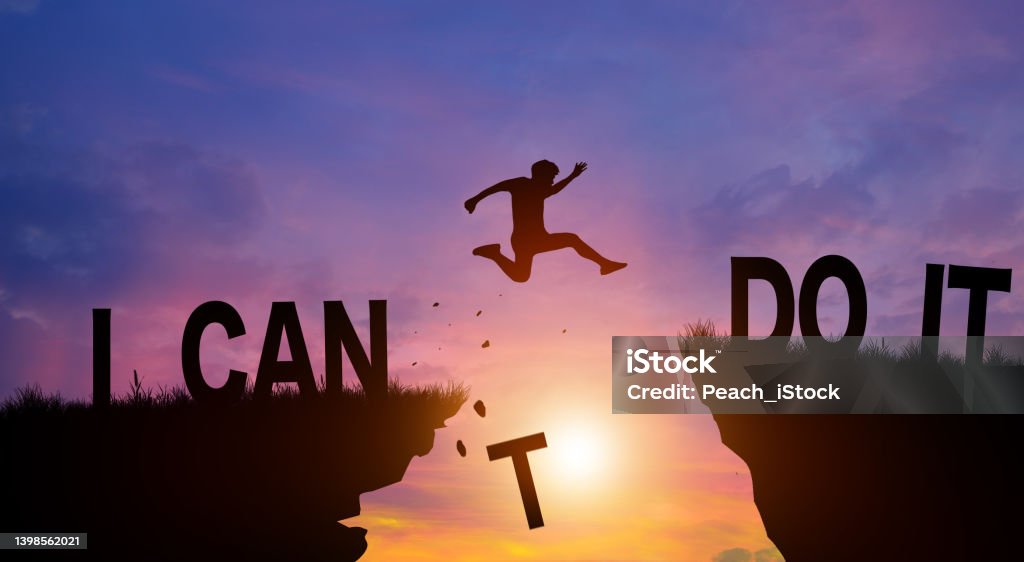 Silhouette man jumping over the cliffs with I can do it word in sunlight. Never give up, Good mindset Concept. Silhouette man jumping over I can do it wording on cliffs with cloud sky and sunrise. Never give up, Good mindset, and Successful achievement Concept. Motivation Stock Photo