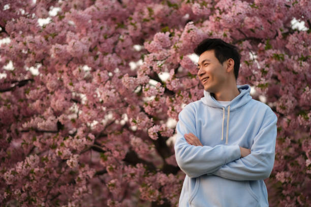 istock smiling Asian young man arm crossing. pink sakura tree background 1398571467