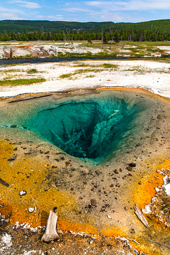 Hot spring and geyser with deep aqua cave and wilderness background at Yellowstone National Park, USA.