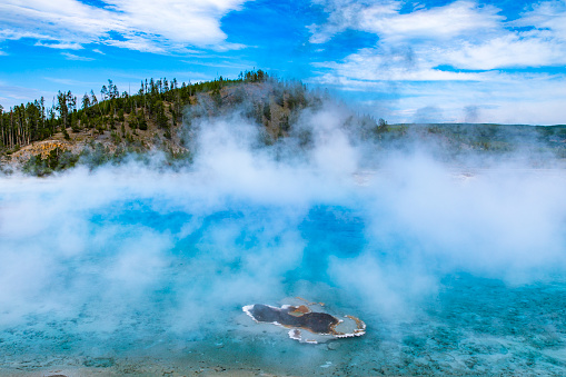 Bright blue clear hot spring with steam coming off the boiling water at Yellowstone national park.