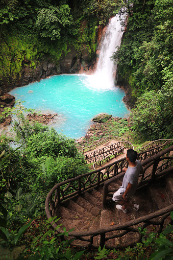 A young man next to the Rio Celeste waterfall in Tenorio Volcano National Park, the northern lowlands of the Guanacaste province Costa Rica. Is famous for its bright blue color water.