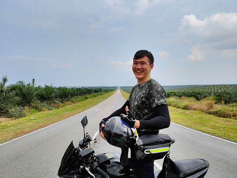 An Asian man is feeling accomplished riding motorcycle on road trip.