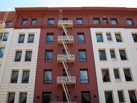 A Fire Escape in downtown San Francisco.  The building is red on the section with the fire escape and off-white on the rest of it.  The fire escape stands out, snaking up the center.