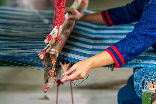 Craftsmen of Thai indigo cotton. Hand of young woman weaving silk in traditional way at manual loom. Sakon Nakhon, Thailand.