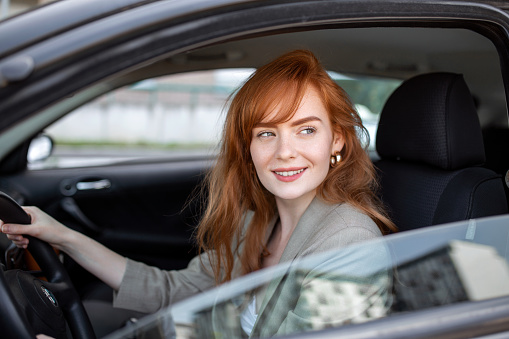 Cute young lady happy driving car. Image of beautiful young woman driving a car and smiling. Portrait of happy female driver steering car with safety belt