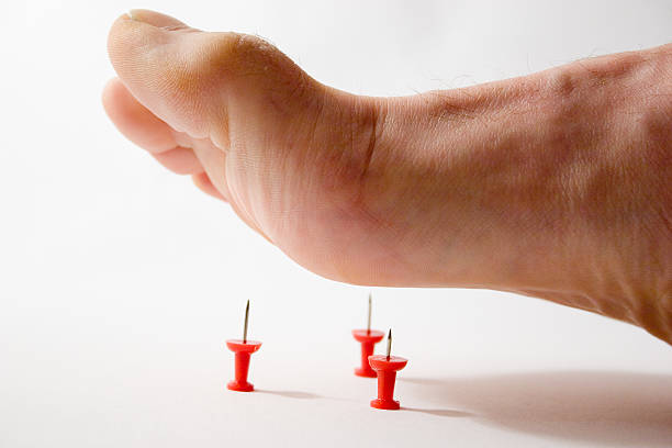 Close up of foot about to step on thumbtacks stock photo