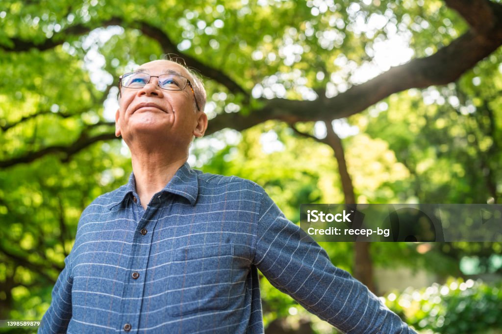Portrait of senior man with her arms raised taking deep breath in nature A portrait of a senior man with her arms raised taking a deep breath in nature. Senior Adult Stock Photo
