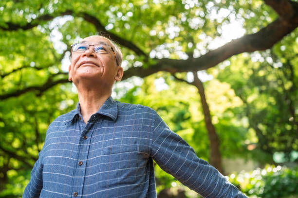 Portrait of senior man with her arms raised taking deep breath in nature stock photo
