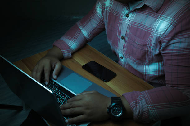 A man is sitting on a laptop in a dark room with lights shining down on it.internet concept addiction.topview. A man is sitting on a laptop in a dark room with lights shining down on it.internet concept addiction.topview. grooming animal behavior stock pictures, royalty-free photos & images