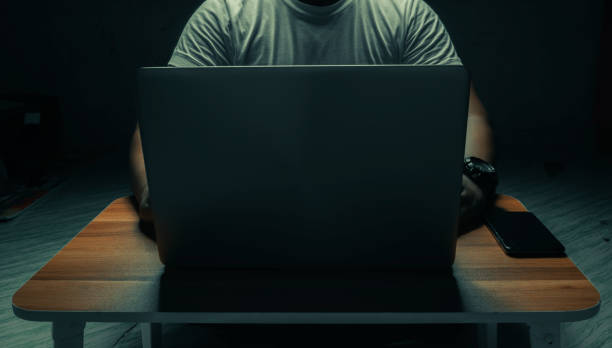 un hombre con una camisa blanca se sienta en una computadora portátil en una habitación oscura. con la luz brillando hacia abajo. concepto internet addiction.topview. - grooming fotografías e imágenes de stock