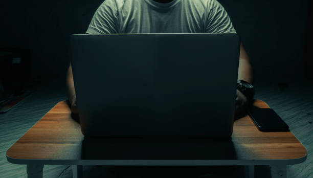 흰색 셔츠를 입은 한 남자가 어두운 방에 있는 노트북에 앉아 있다. 빛이 비추고 있습니다. 인터넷 개념 addiction.topview. - paedophilia 뉴스 사진 이미지