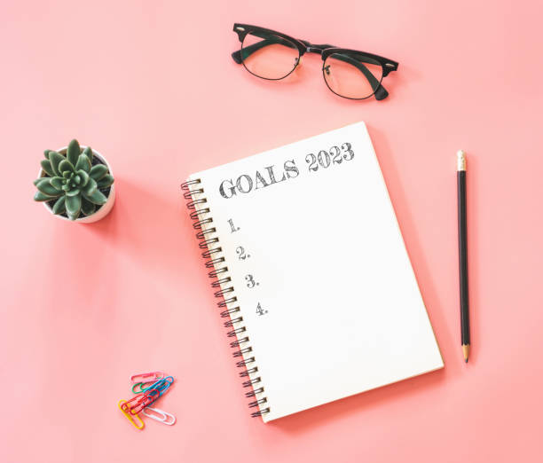 istock Design of workspace desk with blank notebook, with empty goals for 2023 year and phone on color background 1398592473