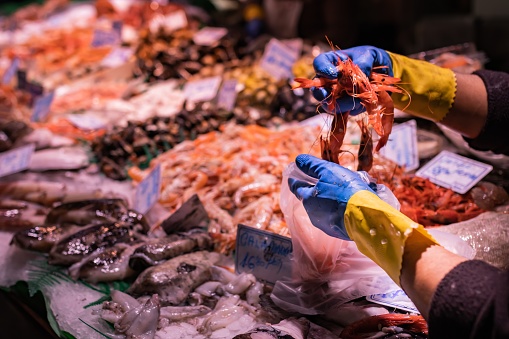 Unrecognizable fishmonger woman selling shrimp in a bag at the market in Vigo (Spain), selective focus on the left hand glove.