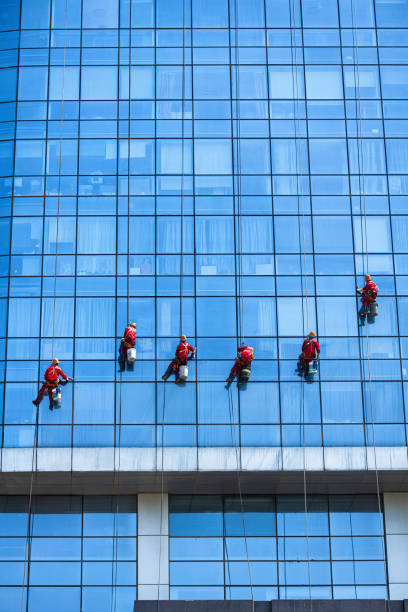 istock Man washing washing office building windows while hanging from ropes 1398597171