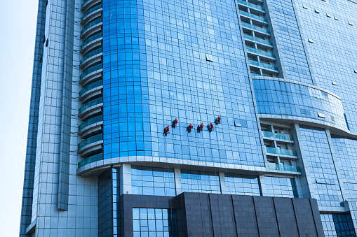 Man washing washing office building windows while hanging from ropes