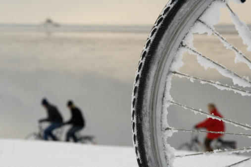 Some people riding their bicylce through the snow on a Northsea-island. The ferry is seen at the horizon.