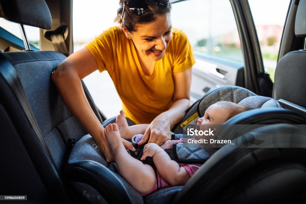 Mother putting baby girl in child seat in car. Family preparing for road trip in summer Mid adult mother putting baby girl in car seat Car Safety Seat Stock Photo