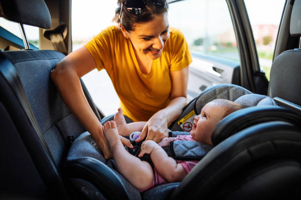 Mother putting baby girl in child seat in car. Family preparing for road trip in summer stock photo