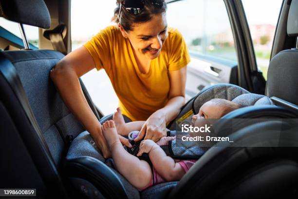 Mother Putting Baby Girl In Child Seat In Car Family Preparing For Road Trip In Summer Stock Photo - Download Image Now