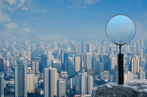 Magnifying glass on rock mountain over modern city tower, office building and skyscraper, Business analyzing concept