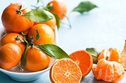 Mandarins (oranges, mandarins, clementines, citrus fruits) with leaves in a plate  on delicate grey background