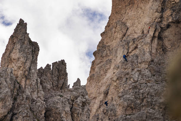 Female mountaineer with backpack, helmet and harness with climbing gear preparing for ascent during summer day in Cinque Torri, Dolomite Alps, Italy - mountaineering or sport climbing concept