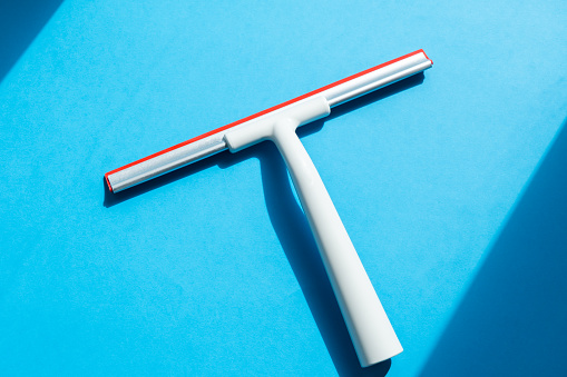 Rubber squeegee for cleaning window on the blue background, concept for spring cleaning, copy space
