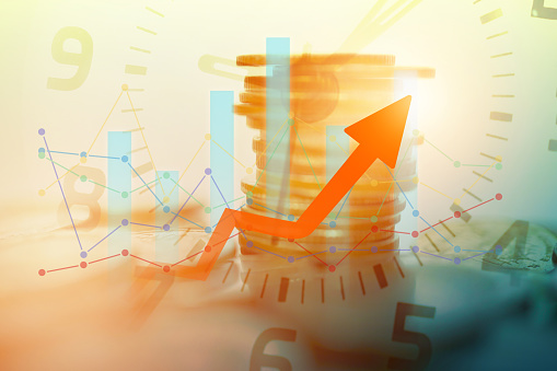 double exposure of stack of coins and clock with graph and arrow for business and finance background