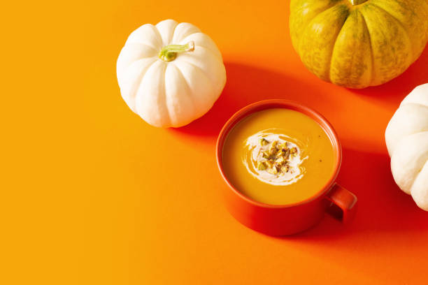 Autumn pumpkins soup with vegetables on orange background, modern concept, copy space