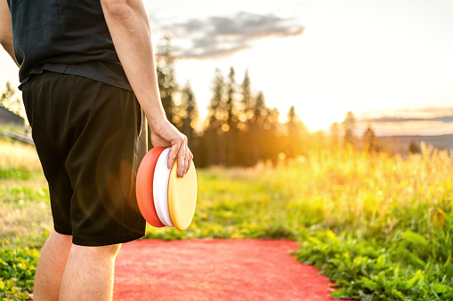 Disc golf in summer at sunset. Man with disc golf equipment in park course. Guy playing discgolf. Player in outdoor sport tournament. Landscape in Finland.