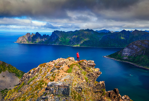 Hiker standing on the top of Husfjellet Mountain on Senja Island in northern Norway and enjoying spectacular views over surrounding fjords and mountains.