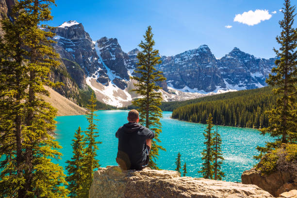 Hiker enjoying the view of Moraine lake in Banff National Park Hiker enjoying the view of Moraine lake in Banff National Park, Alberta, Canada, with snow-covered peaks of canadian Rocky Mountains in the background. rocky mountains banff alberta mountain stock pictures, royalty-free photos & images