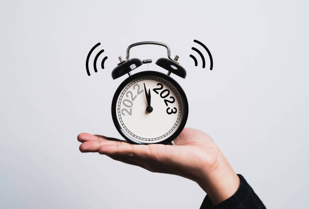 メリークリスマスとハッピーニューイヤーのコンセプトのために、スクリーンの年が2022年と2023年から変わる黒い目覚まし時計を手持ち。 - time clock watch futuristic clock hand ストックフォトと画像