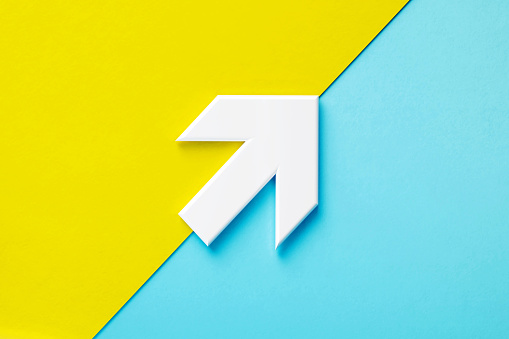 Extruded white up arrow sitting over yellow and blue background. Horizontal composition with copy space.