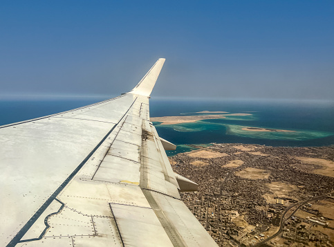Wing of an airplane flying above Red Sea and Hurghada city, Egypt.