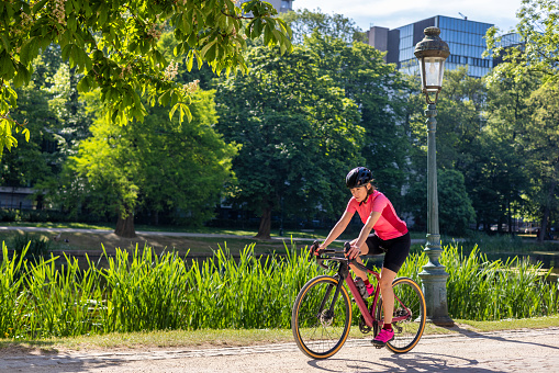 Young woman on a race bike, wearing bright sports wear in an eco urban area city park.\nLocation: Brussels