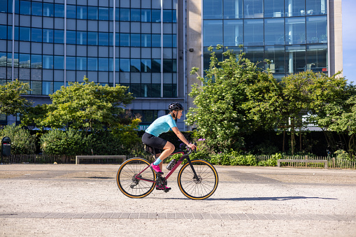 Side view of a woman riding a sports bike in a lush green eco area of the city with trees and buildings in scene.
Copy space provided.
Location: Brussels