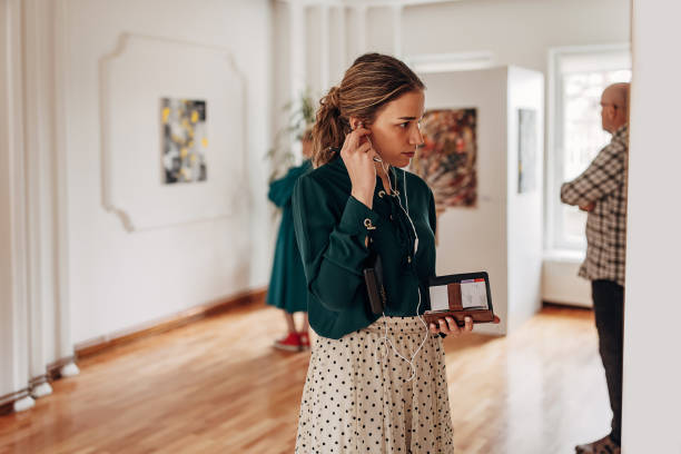 Woman in art gallery Diverse group of visitors in modern art gallery, woman looking at paintings and listening to audio guide on headphones. gallery opening stock pictures, royalty-free photos & images