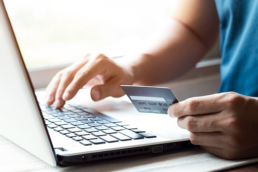 Cheerful young man paying bills online with credit card and laptop.