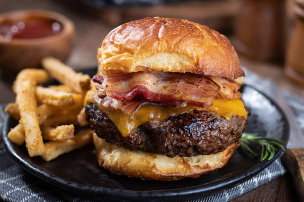 Bacon cheeseburger on a toasted bun Closeup of a bacon cheeseburger on a toasted bun and french fries on a black plate thick photos stock pictures, royalty-free photos & images