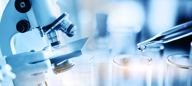 scientist or chemist using microscope with laboratory glassware, science research and development concept, dropping chemical liquid to test tube in lab.