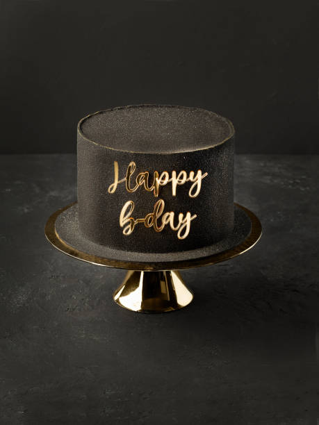 Black birthday cake decorated with golden topper. stock photo