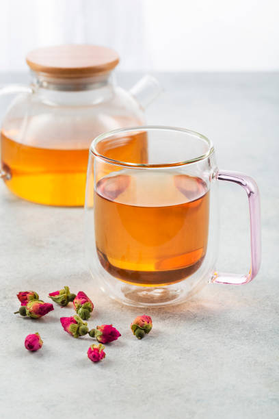 istock Glass cup of tea with teapot and rosebuds on light table against blurred background 1398634713