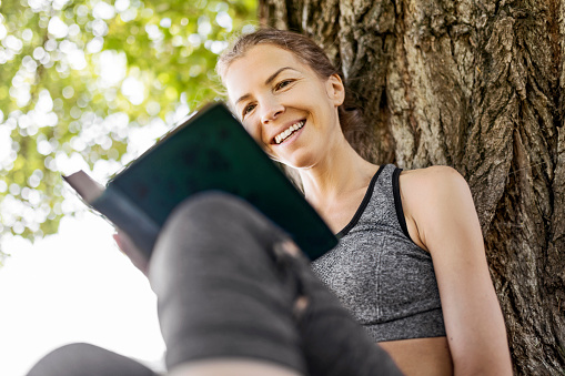 Happy young woman reading a book in public park