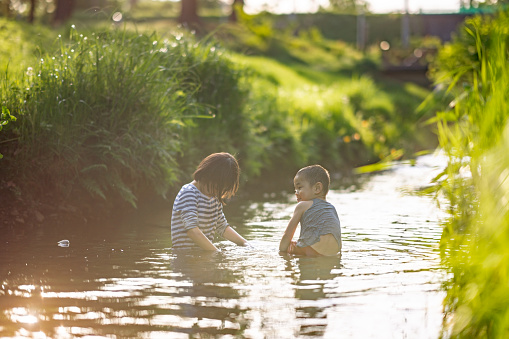 A brother and his sister are playing and having fun in a river in nature.