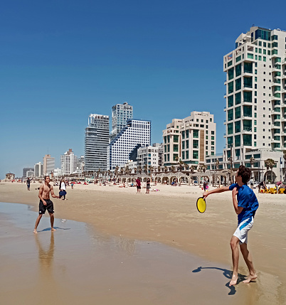 Two guys playing paddles in the beach of Tel Aviv during a sunny spring day. At the back are seen the famous hotels and skyscrapers on the \