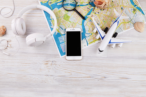 Accessories for travelers: phone, headphones, magnifying glass, map, shells and airplane on a wooden background. Travel concept. Planning summer holidays. Flat lay. Copy space.