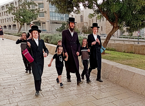 An ultra-orthodox man from the Haredi jewish comunity walking together with his children in the streets of Jerusalem during the Festival of Sukkot.\nHasidic Jewish people are known for having large families. 6-10 children is typical, and sometimes they have as many as 12 or more!